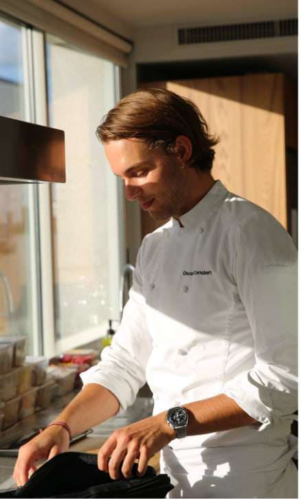 Le chef Oscar Cornubert, en veste blanche, au travail devant une baie vitrée.
