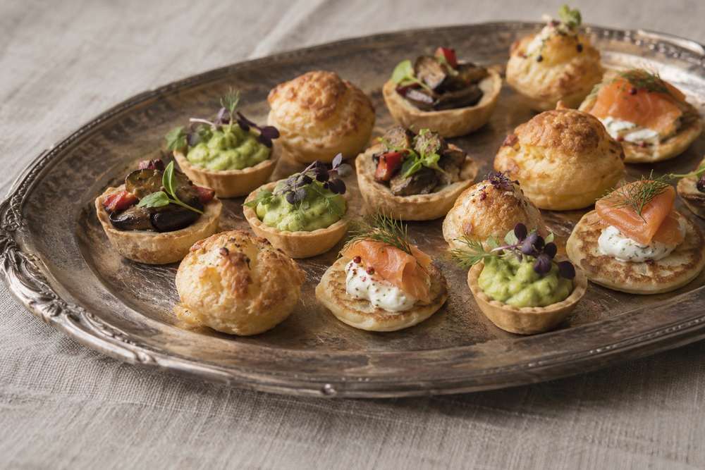 Tartelettes végétales, gougères et blinis au poisson fumé sur un plateau argenté.